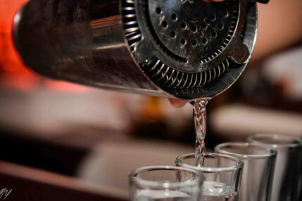 Shaker pouring liquior on various glasses